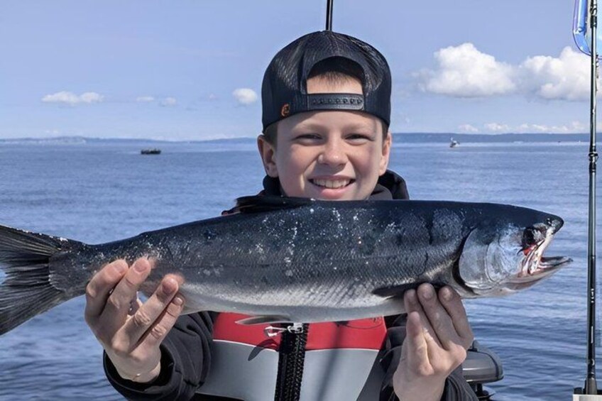 A person holding a fish by a body of water with a fishing rod in the background. 2