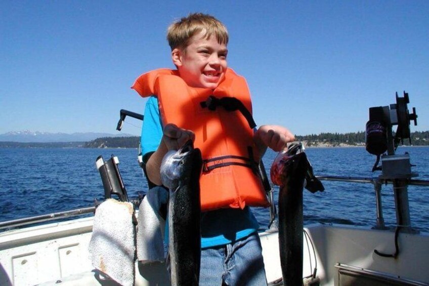A person on a boat holding a fish, wearing a life jacket, with a clear sky and water in the background. 5