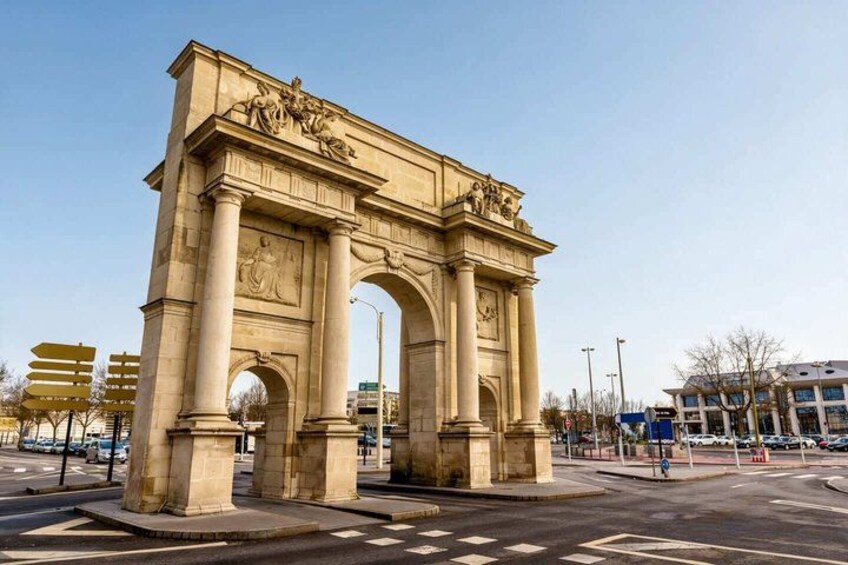 A large stone arch monument with columns and sculptures, located at a city intersection. 4