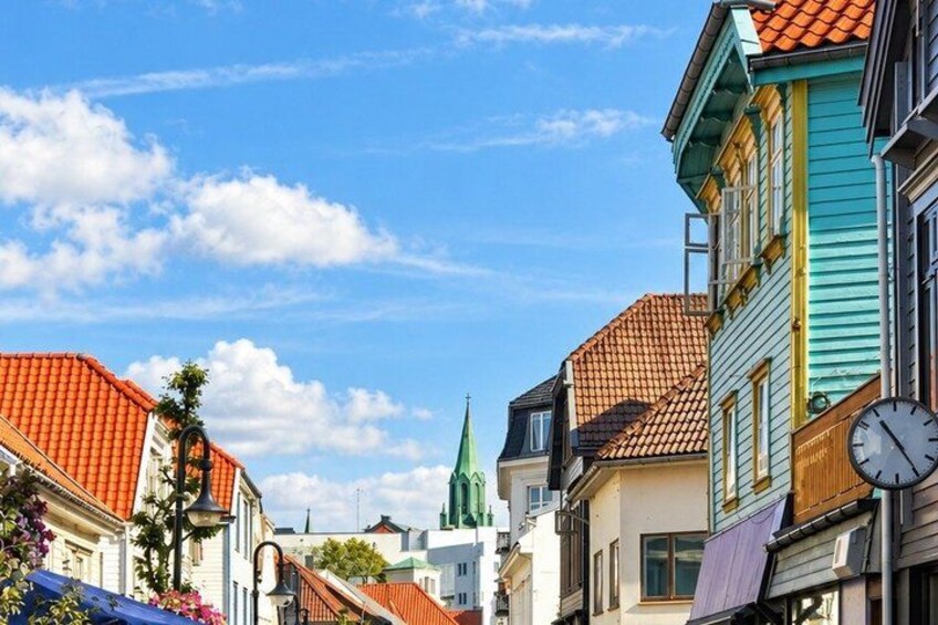 A street with colorful buildings, a clock, and a church spire in the distance. 1