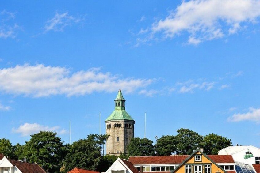 A tower with a green roof, surrounded by houses with red roofs and a clear blue sky. 2
