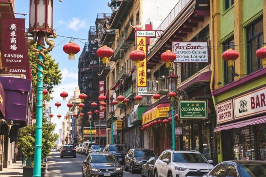 A street lined with shops, red lanterns, and parked cars. 2