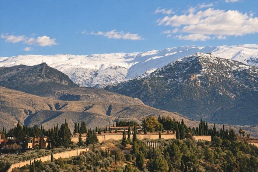 A mountainous landscape with snow-capped peaks, a clear sky, and scattered trees. 1
