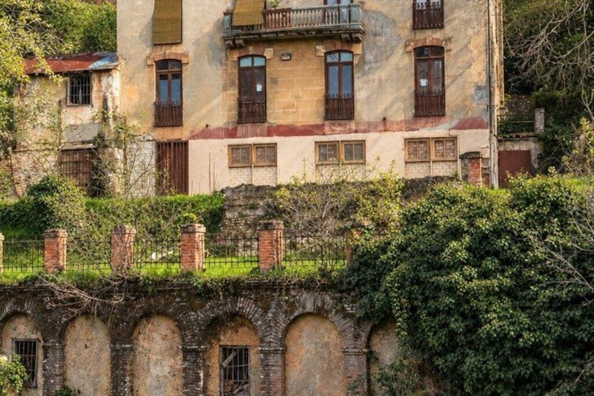 A historic building with arched windows and a balcony, surrounded by greenery. 2