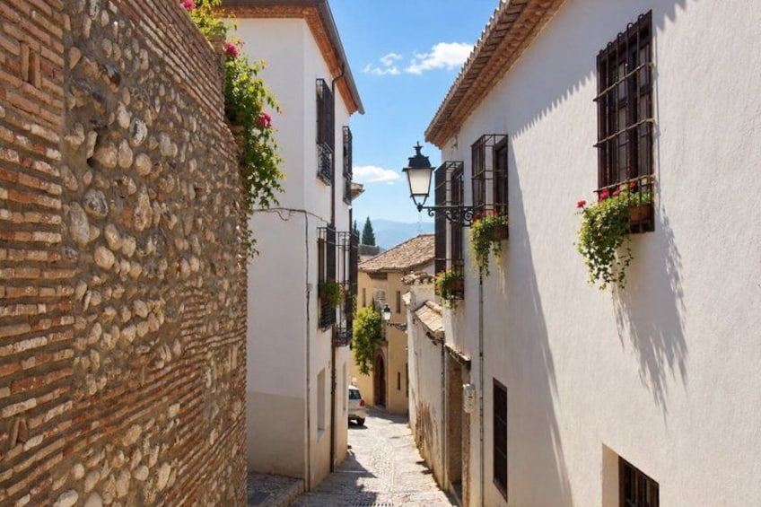 A narrow cobblestone street flanked by buildings with stone walls and white plaster exteriors, under a clear sky. 3