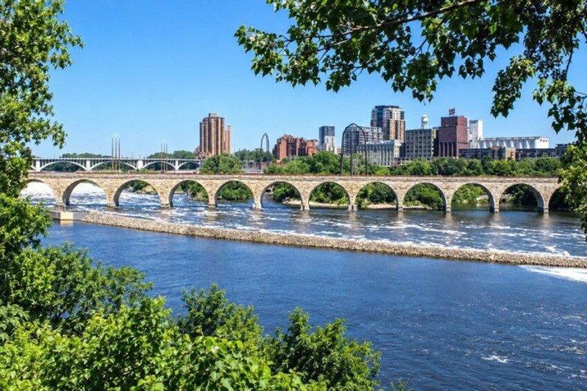 A river with a stone bridge, city skyline, and greenery. 3