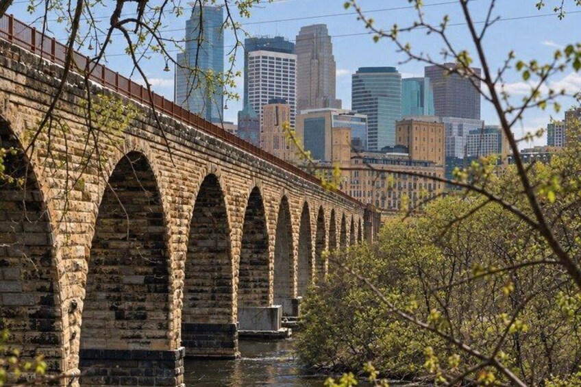 A stone bridge with multiple arches over a body of water, with a city skyline in the background. 2