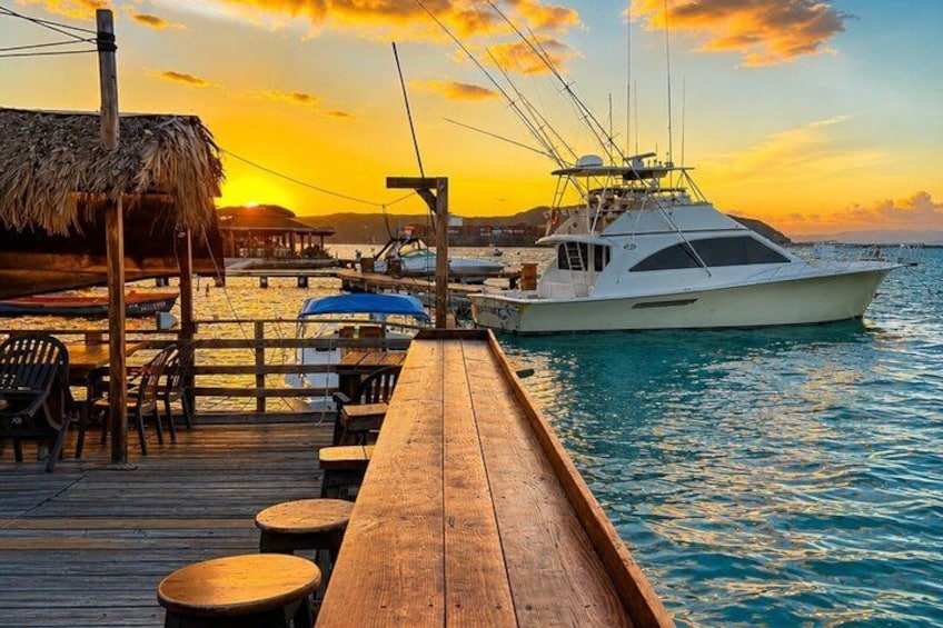 A wooden pier extending into calm waters at sunset, with a white boat docked at the end. 5