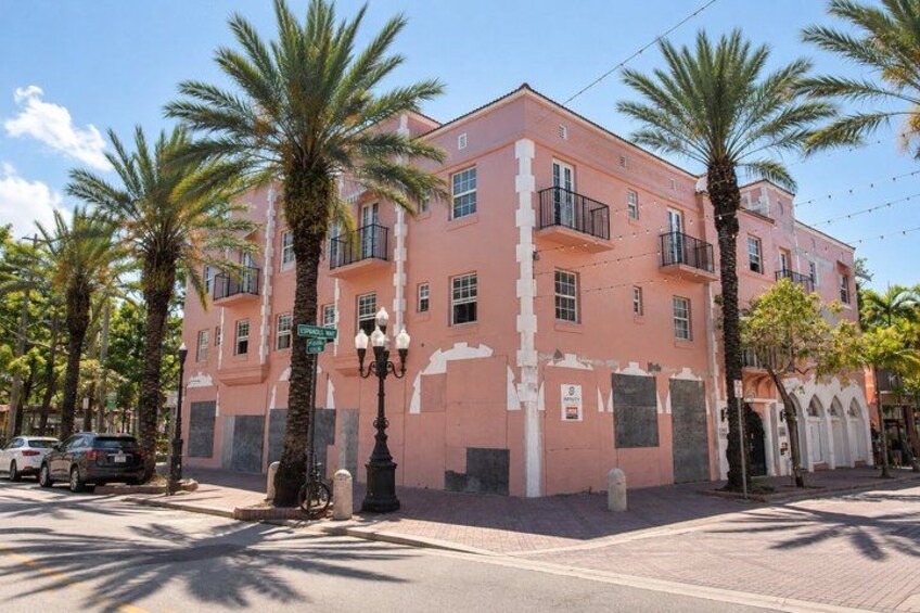 A pink building with balconies, palm trees, and a street lamp. 3
