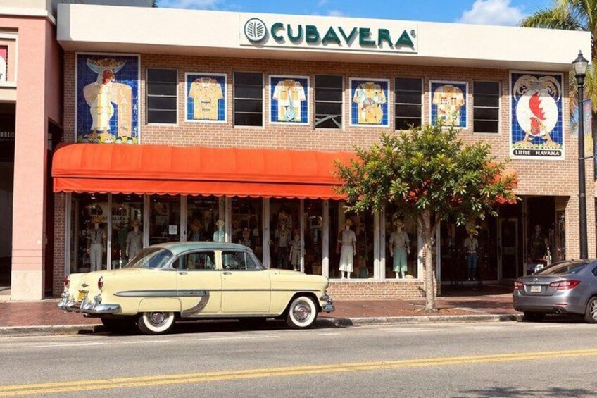 A vintage car parked in front of a building with a red awning and Cuban-themed murals. 4