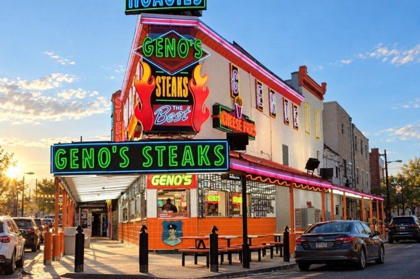 A restaurant named Geno's Steaks with neon signs and a red awning. 5