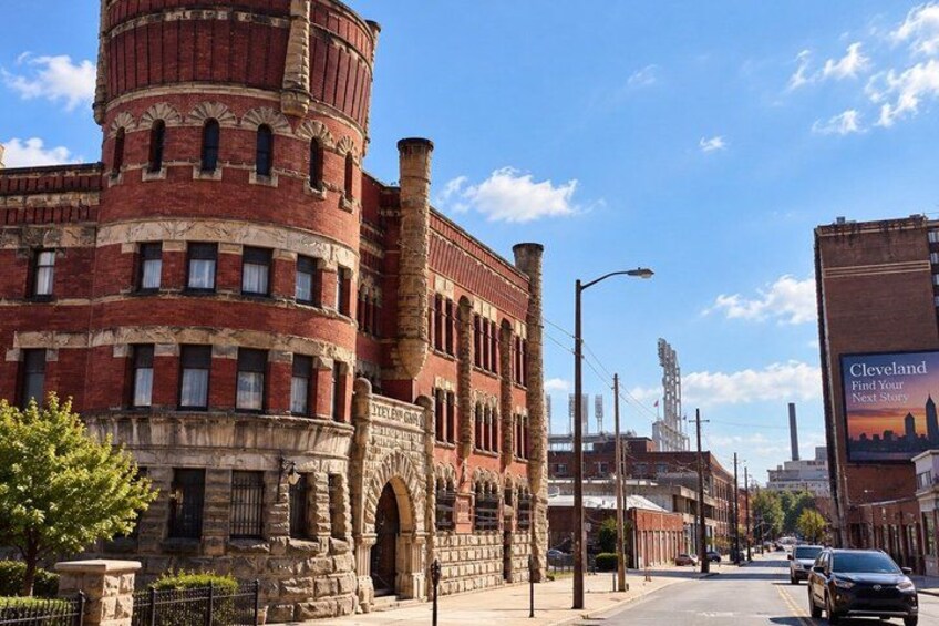 A historic brick building with arched windows and a cylindrical tower, a street with cars, and a clear blue sky. 4