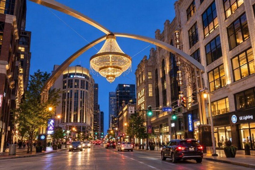 A city street at dusk with a prominent illuminated chandelier, buildings, and traffic lights. 3