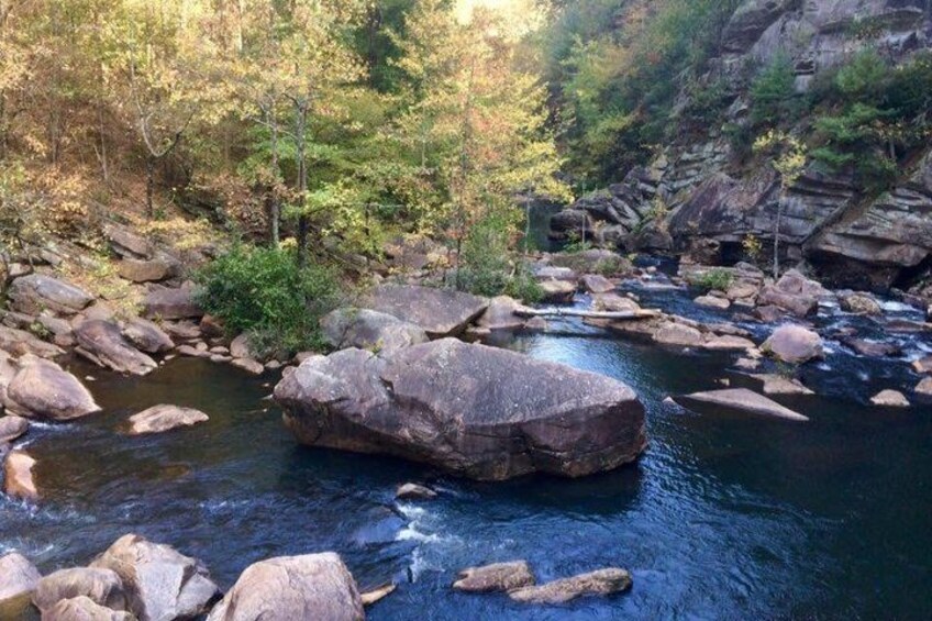 A river with large rocks, surrounded by trees and rocky cliffs. 4
