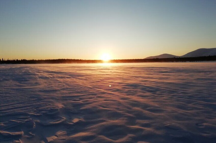 A frozen landscape with the sun setting over a snow-covered field and distant mountains. 5