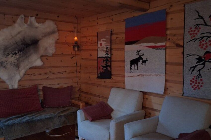 A cabin interior with wooden walls, a fur rug, a white armchair, and wall art depicting nature scenes. 3
