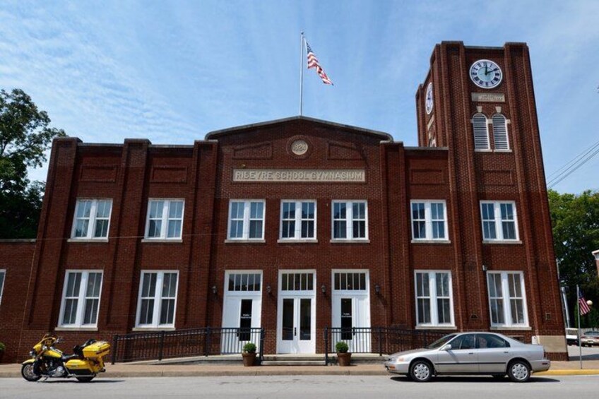 A brick building with a clock tower, a flag, and a sign that reads 'Riley School of Music.' 5