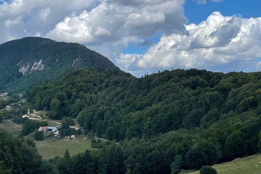 A mountainous landscape with dense forests, a small village, and a prominent hill with rocky outcrops. 5