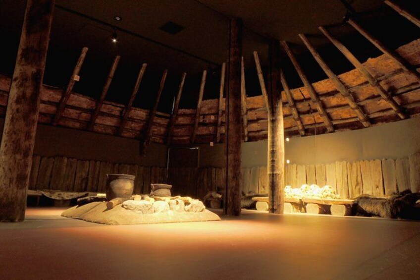 A rustic interior with a wooden ceiling, a large stone fireplace, and a table with a pile of bread. 3