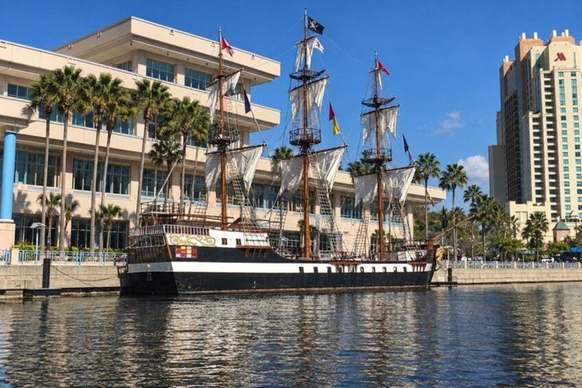 A tall ship docked at a marina with palm trees and modern buildings in the background. 5