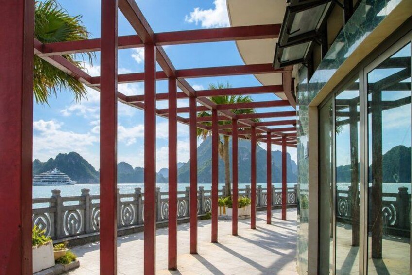 A balcony with red metal railings, a glass door, and a view of a cruise ship and mountains in the distance. 4