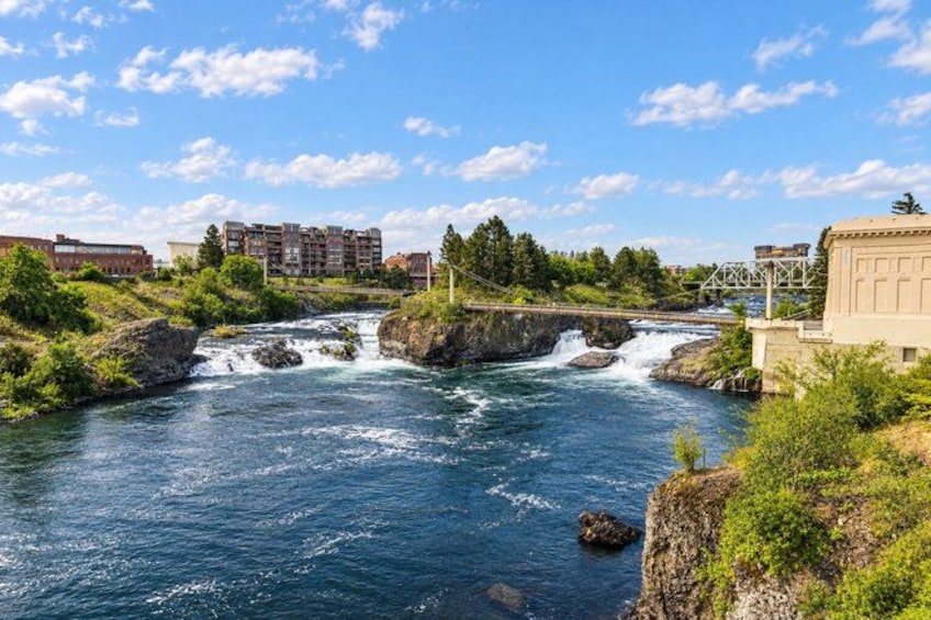 A river with rapids, a bridge, and buildings in the background. 1