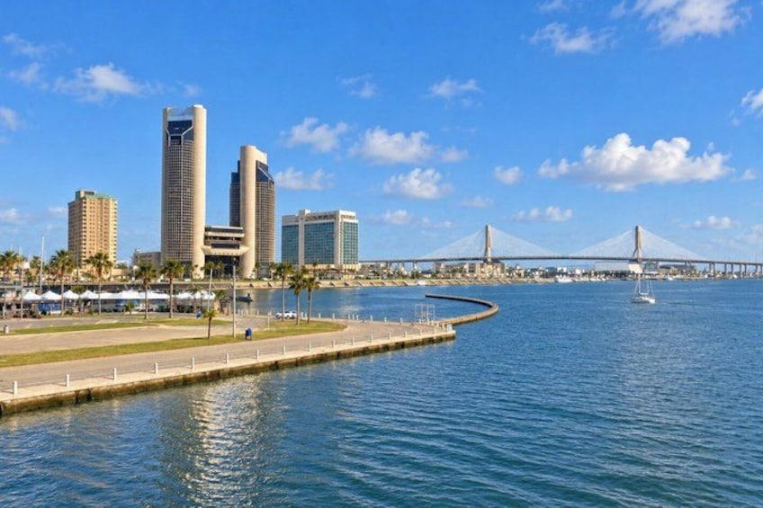 A waterfront cityscape with modern buildings, a bridge, and calm water. 2
