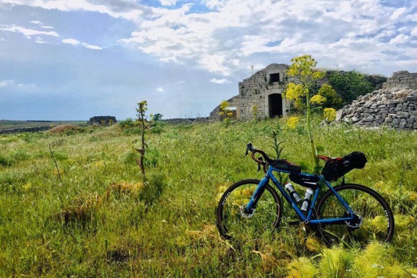 A bicycle in a grassy field with a stone building in the background. 1