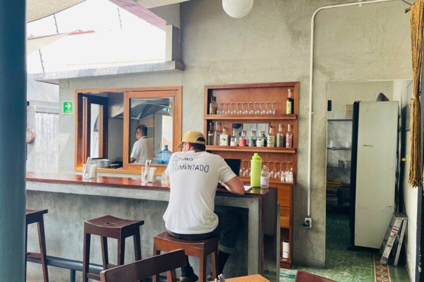 A person working behind a bar counter in a restaurant with wooden shelves and a refrigerator. 2