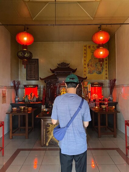 A person standing in a temple with red lanterns, incense burners, and religious statues. 2