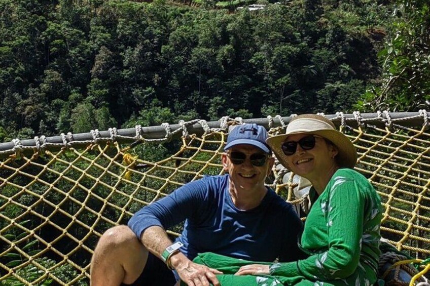 Two people sitting on a rope bridge with a forested background. 2