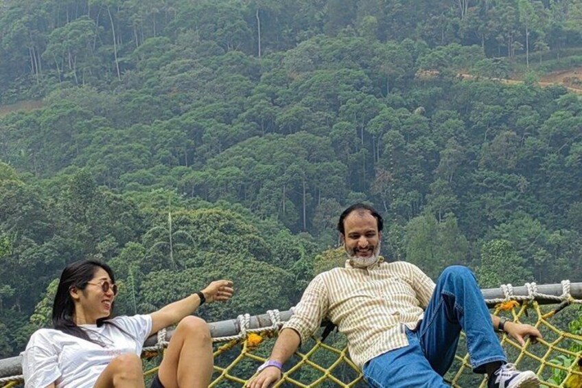 Two people sitting on a rope barrier with a forested hill in the background. 3
