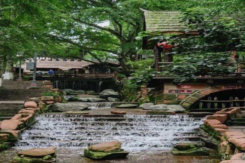 A traditional stone waterway with steps leading down to a small waterfall, surrounded by lush greenery and traditional architecture. 5
