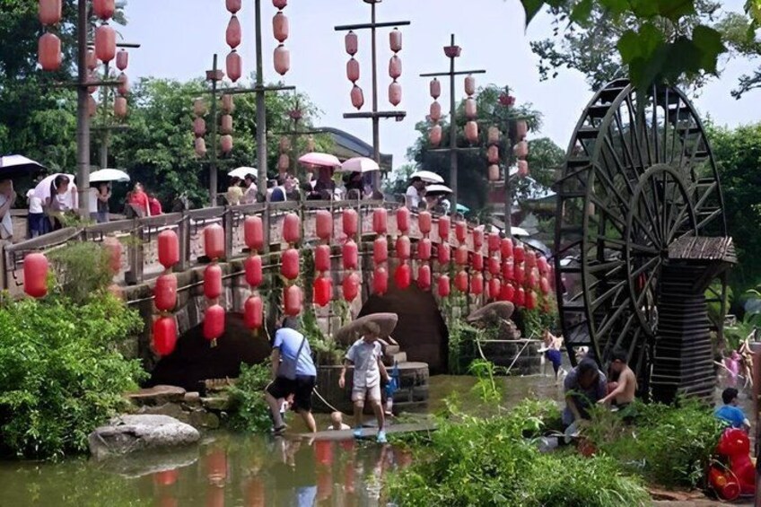 A traditional water wheel, a stone bridge with red lanterns, and a pond with people around. 2