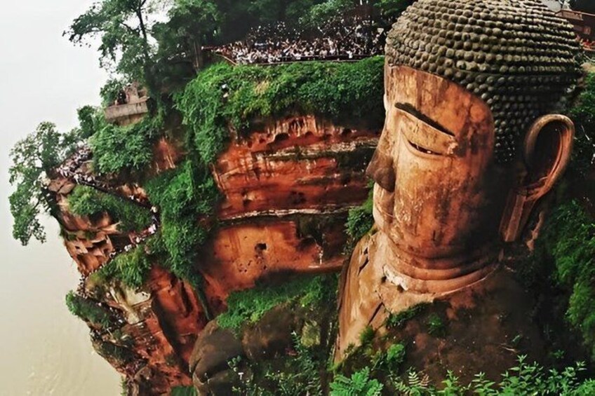 A large Buddha statue on a cliff with lush greenery. 1