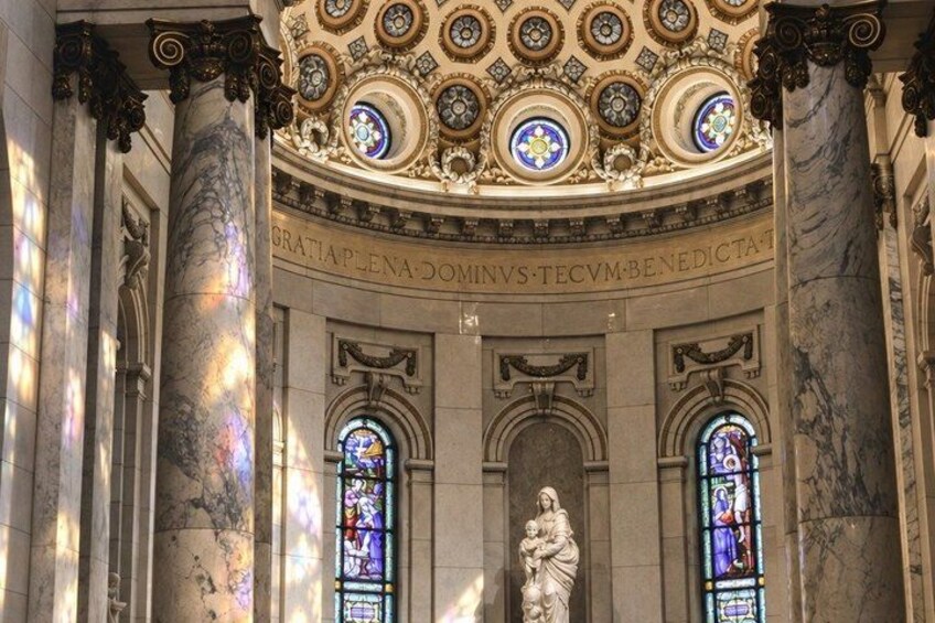 A grand architectural interior with ornate ceiling designs, stained glass windows, and a central statue. 2