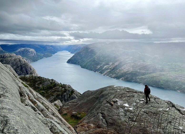 A person standing on a rocky mountain ridge overlooking a deep valley with a lake. 5
