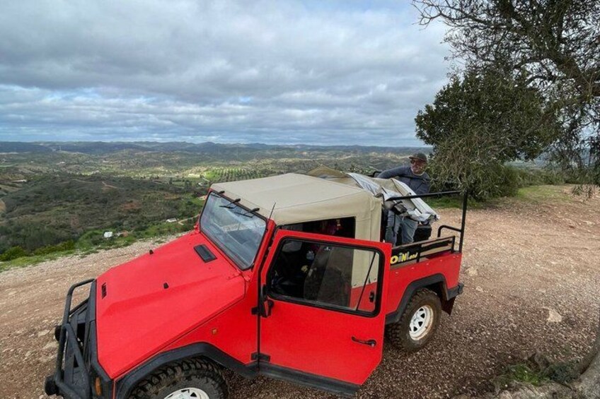 A red off-road vehicle parked on a dirt path with a person standing in the back. 3