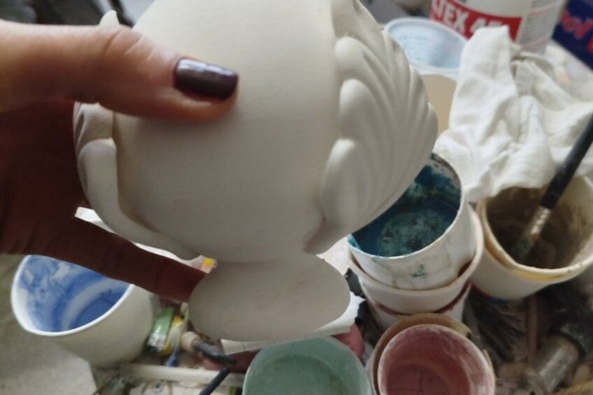 A hand holding a white ceramic object with a blue paintbrush nearby. 3