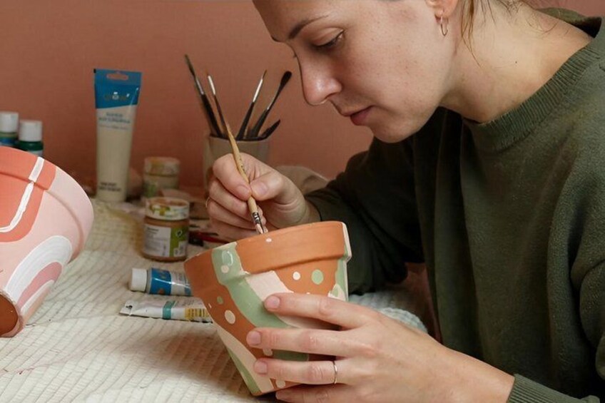 A person painting a terracotta pot with polka dots. 1