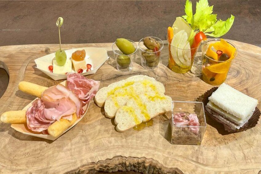 A wooden board with various food items including cheese, meats, bread, and drinks. 5