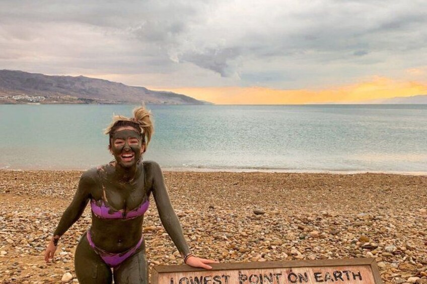 Une personne se tient sur une plage de galets, à côté d’un panneau indiquant : « POINT LE PLUS BAS DE LA TERRE ». 2