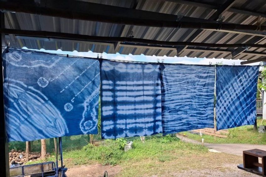 A covered outdoor area with blue patterned fabric screens, a dirt path, and some greenery. 4