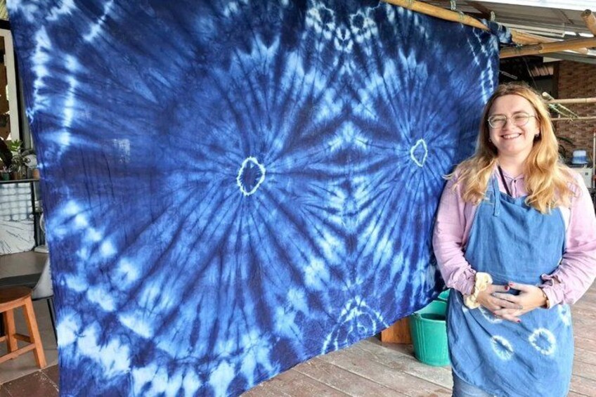 A person standing in front of a large blue tie-dye fabric with a circular pattern. 1