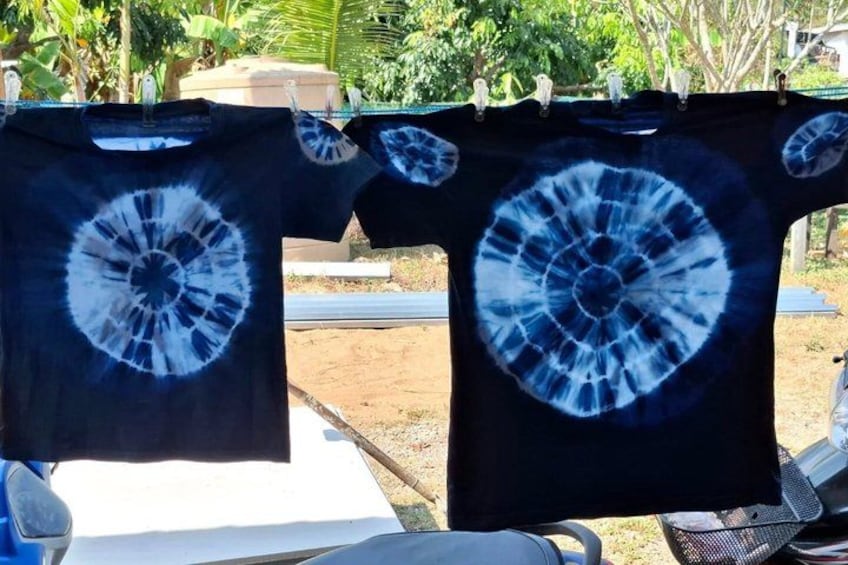 Two black t-shirts with a blue tie-dye pattern hanging on a clothesline outdoors. 3