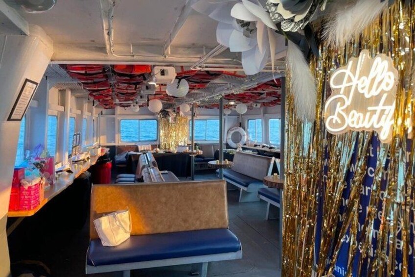 A ship's interior with seating, a bar area, and decorative elements like a neon sign and tinsel. 2