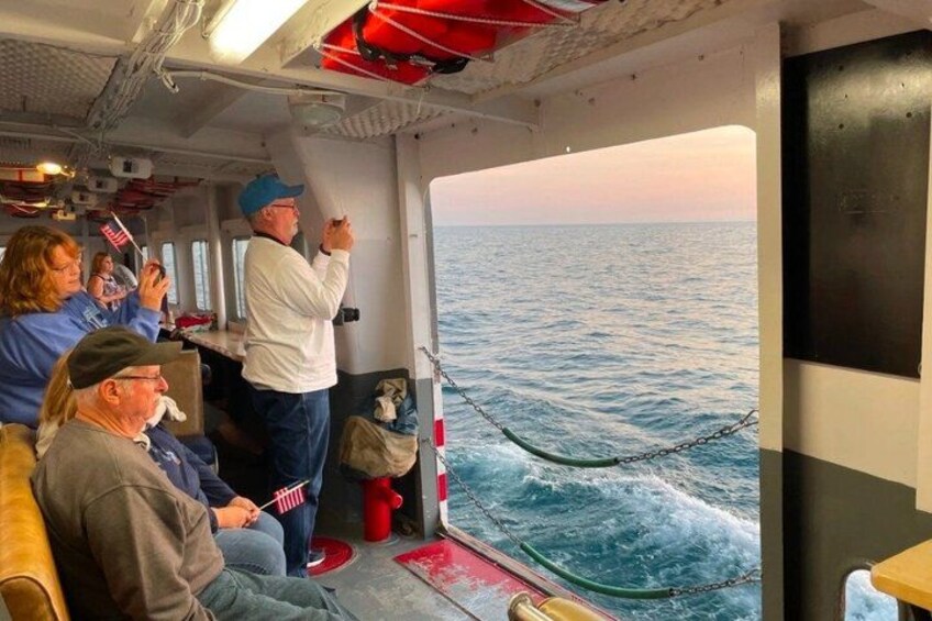 A boat with people on deck, some taking photos, and a view of the ocean. 5
