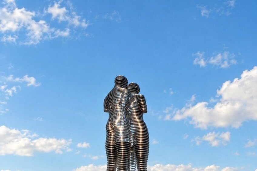 A metallic sculpture of a human figure against a clear blue sky. 3