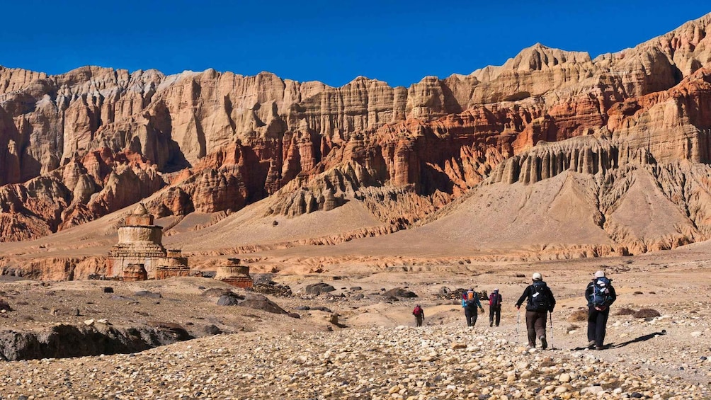 Paisaje desértico rocoso con una pequeña construcción de piedra y excursionistas. 1
