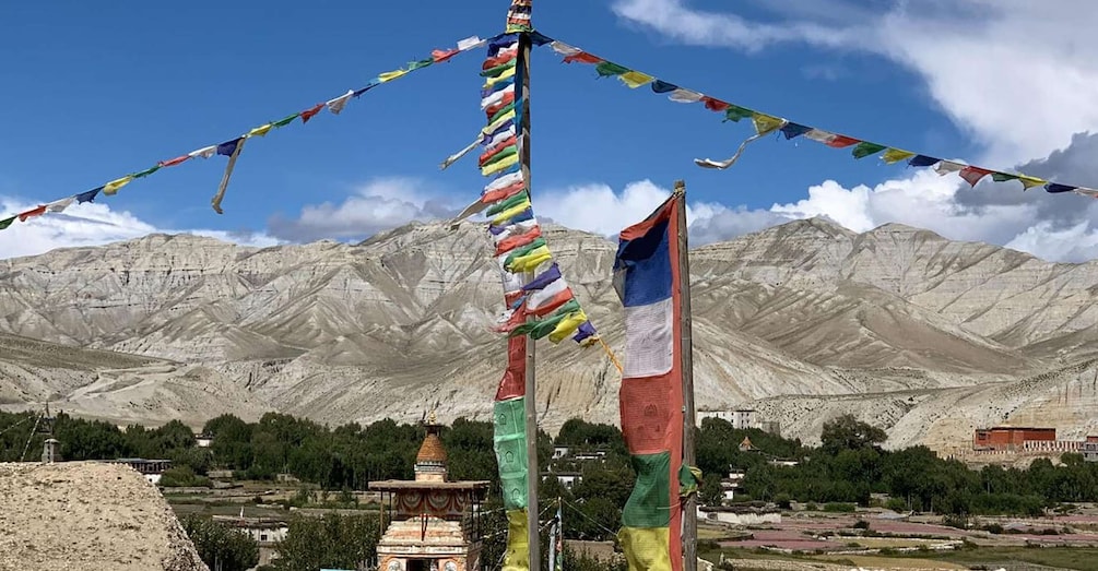 Un paisaje montañoso con cielo despejado, un edificio tradicional y vibrantes oraciones en banderas de colores. 2